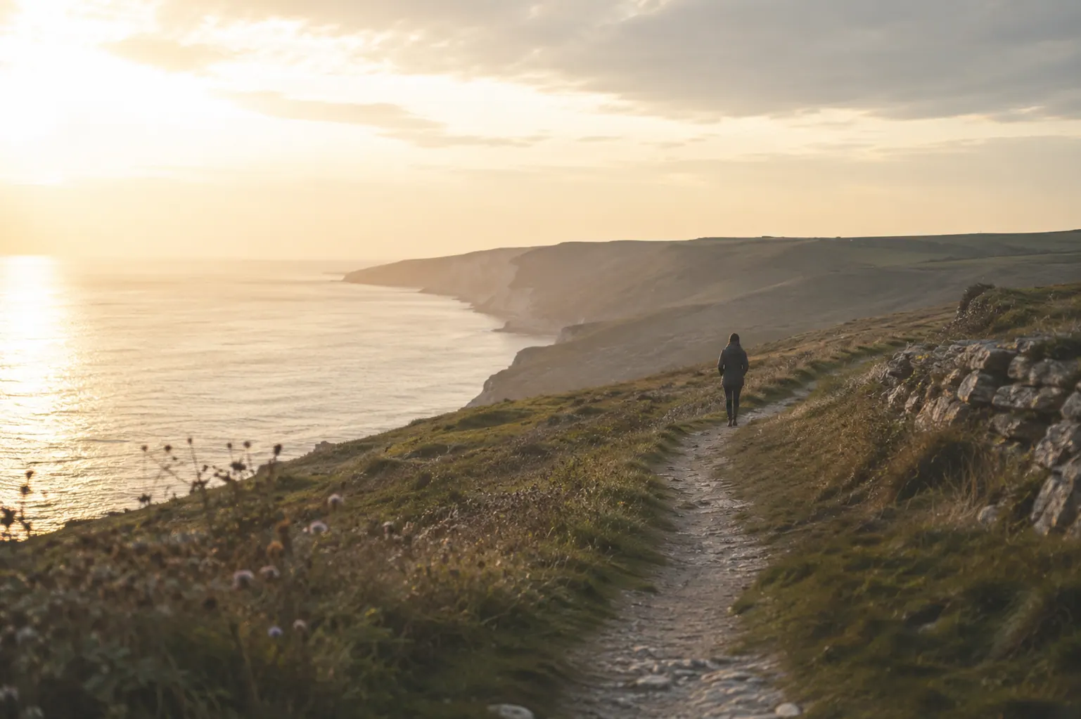 A person walking along a quiet coastal path in warm evening light